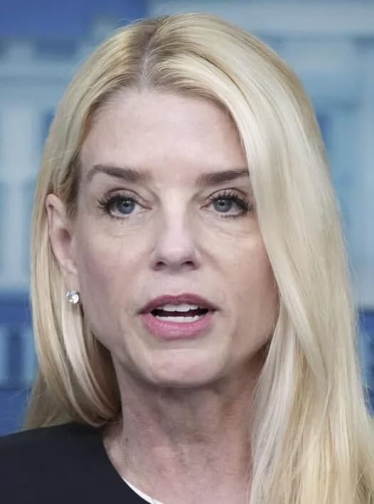 Close portrait photograph of blonde woman Pam Bondi speaking, against a blurred blue-and-white official backdrop