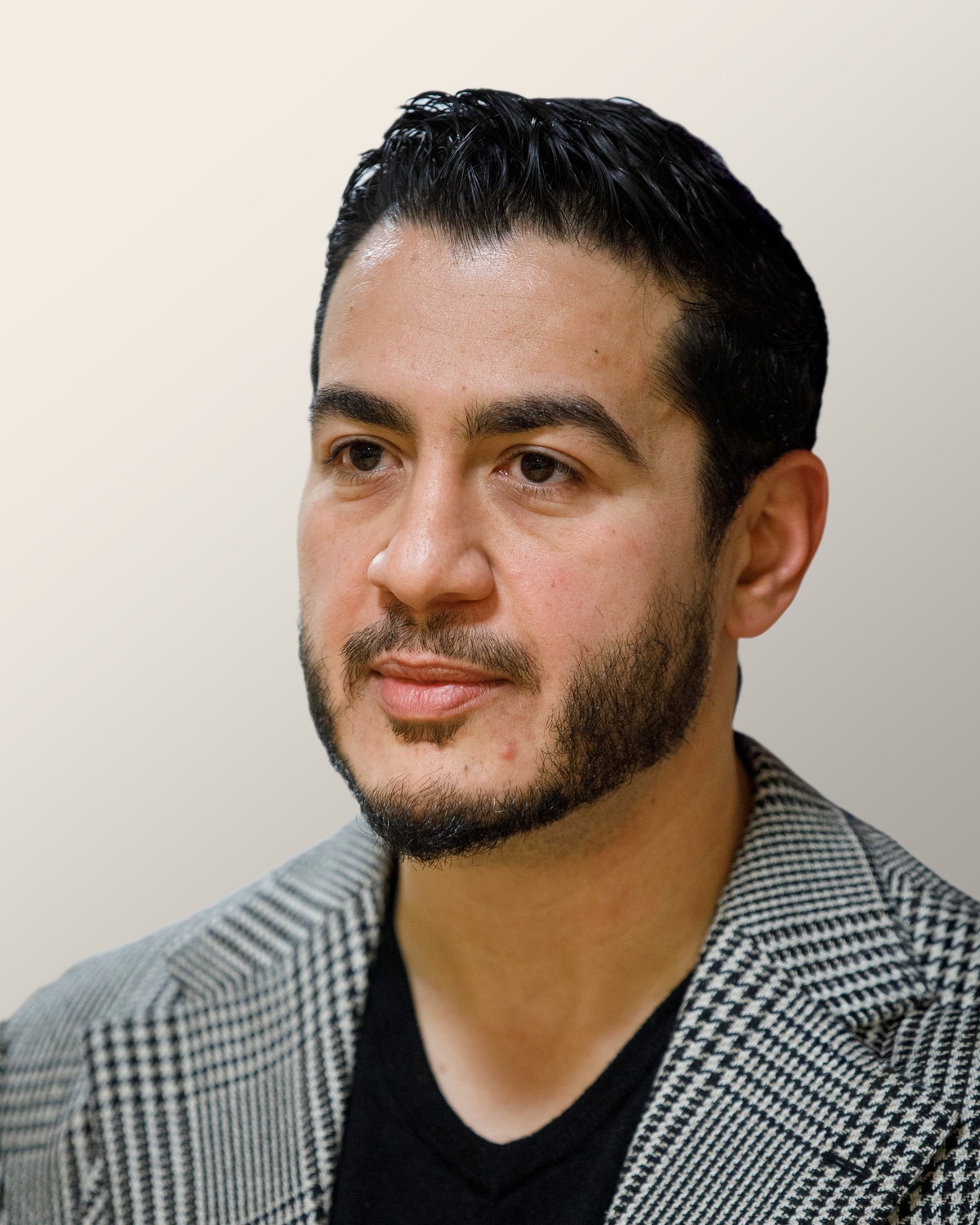 Portrait of Abdul El-Sayed in a checked blazer over a black shirt, looking to his right against a plain wall.